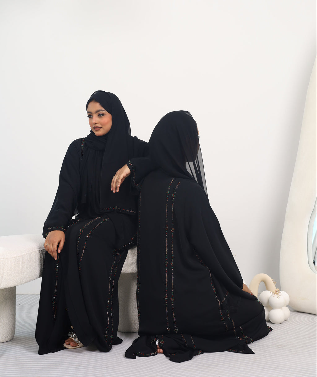 Person wearing a black outfit with a hood in a minimalistic setting