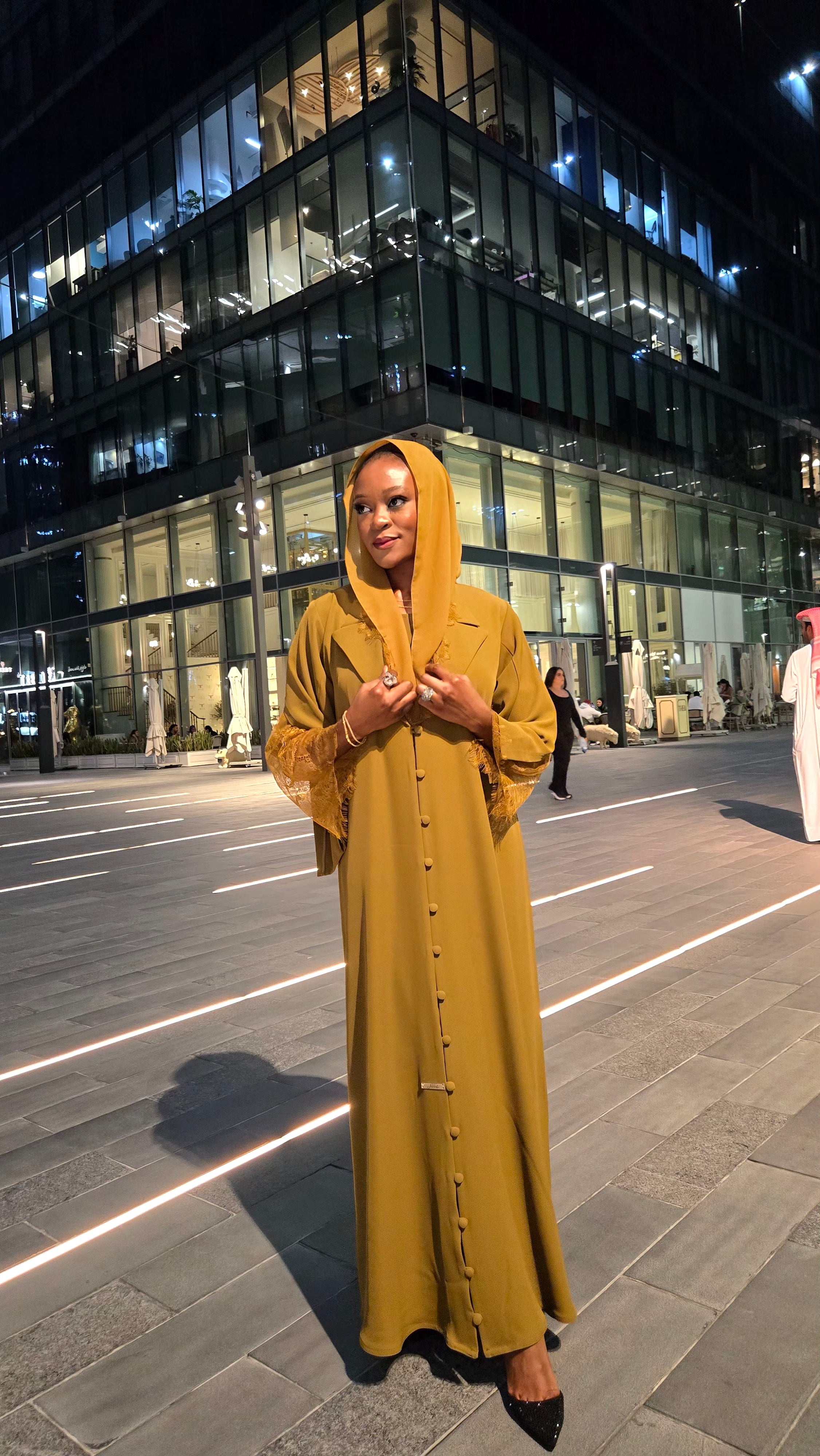 Woman in a mustard yellow dress standing on a city street at night.