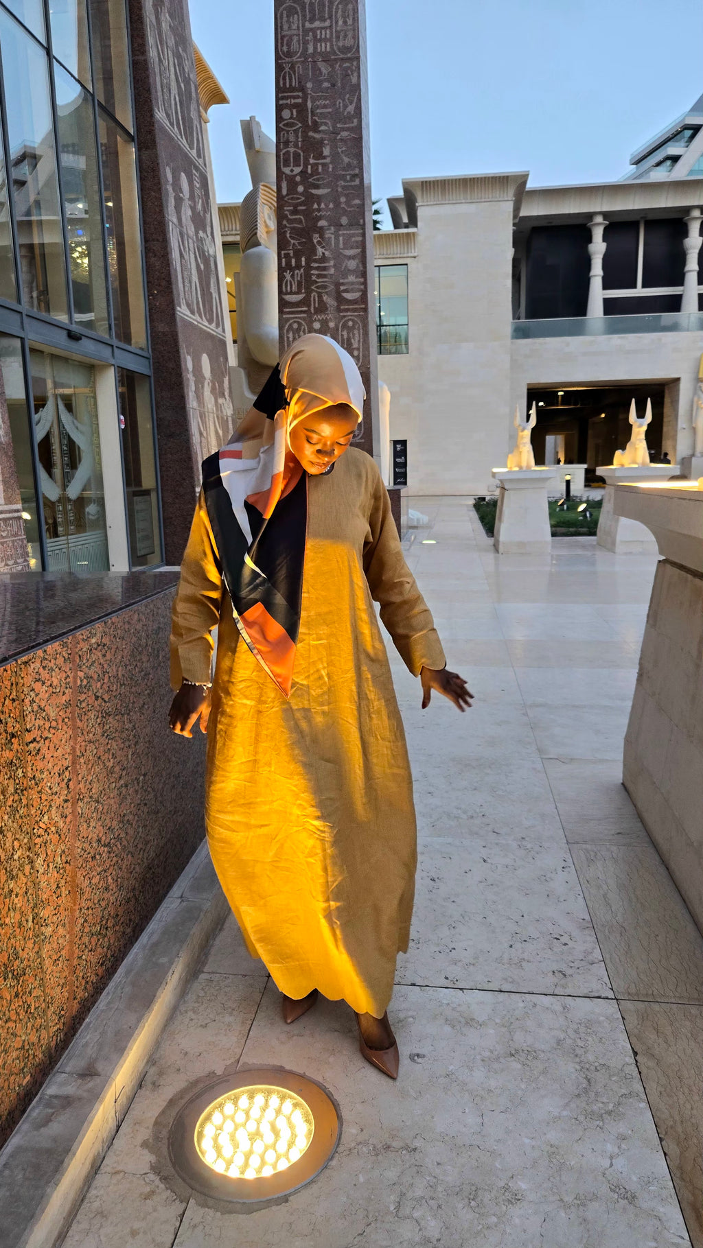 Woman in a long, light-colored dress with a yellow skirt walking outdoors.
